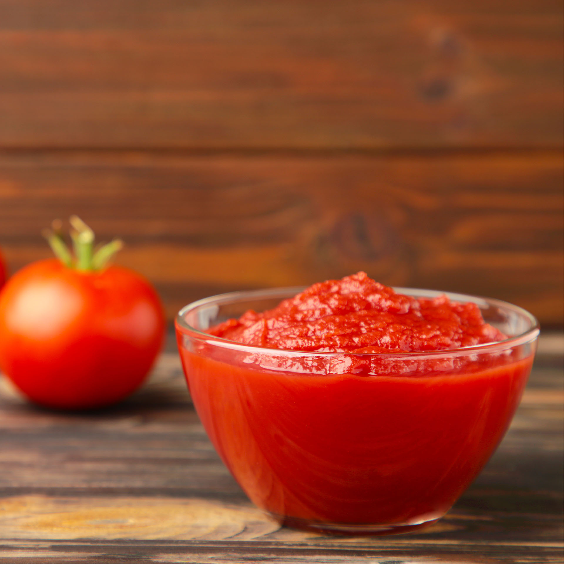 Tomato ketchup sauce in a bowl with tomatoes on brown wooden background.