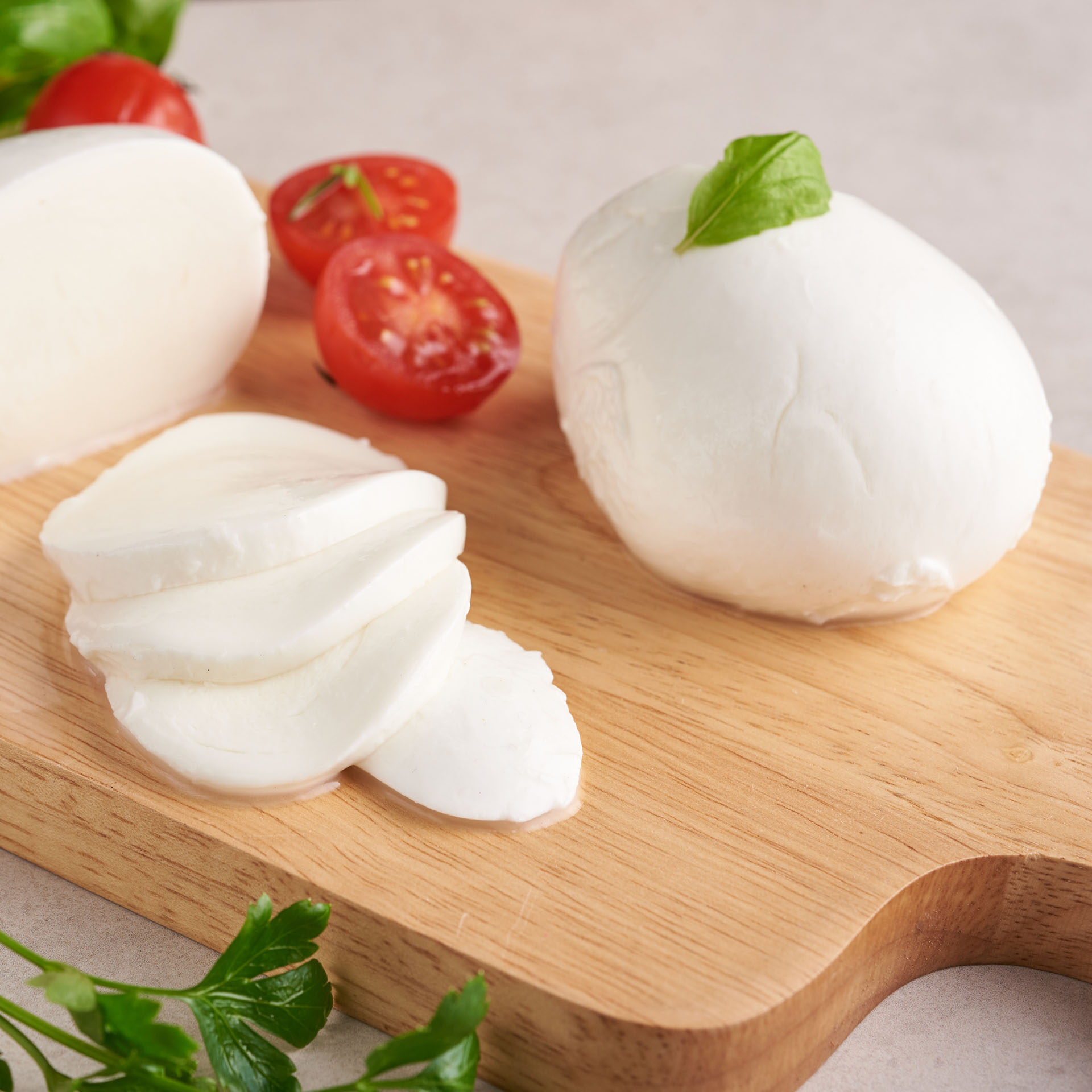 Fresh mozzarella cheese, Soft italian cheeses, tomato and basil, olives oil and rosemary on wooden serving board over light wooden background. Healthy food. Top view. Flat lay.